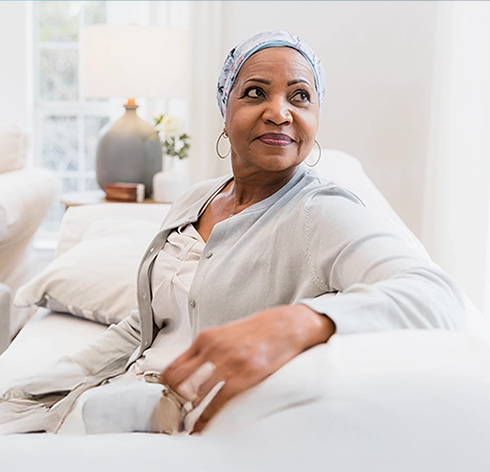 A woman wearing a headscarf sitting on a sofa and looking hopeful, symbolizing TNBC resilience in Canada